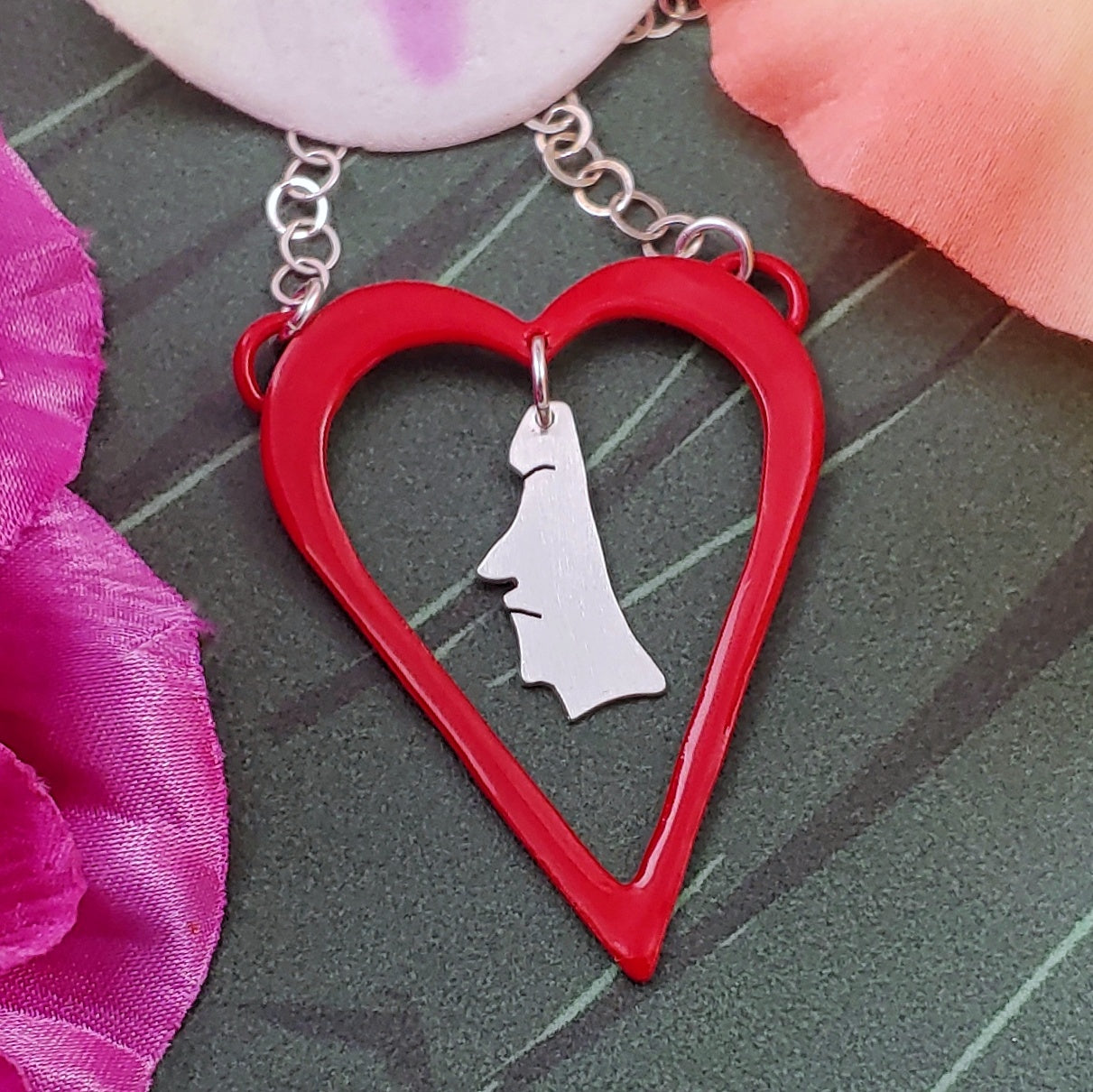 Powdercoated red heart shaped necklace with sterling silver moai dangling from the center