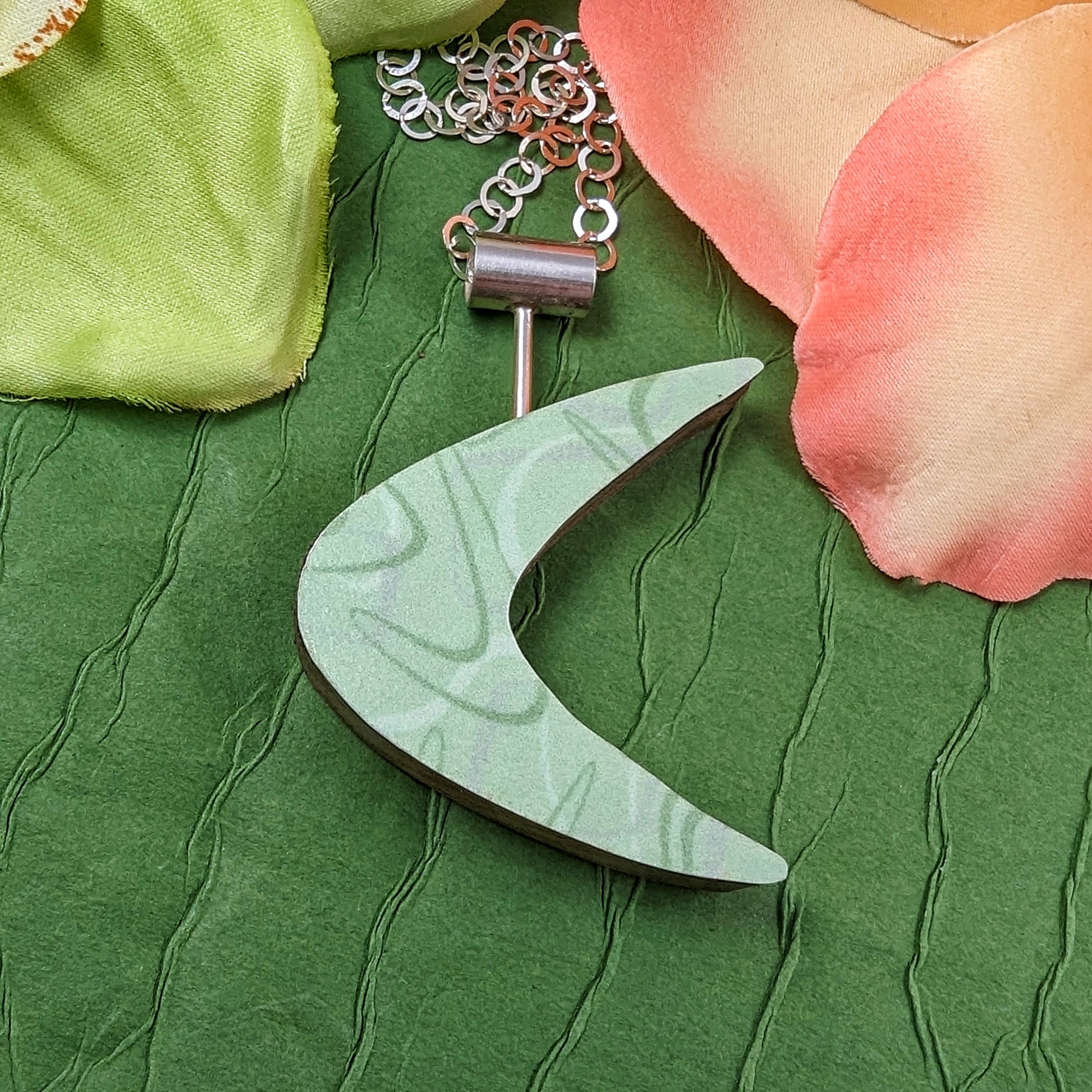 Boomerang shaped laminate on wood necklace on a green background