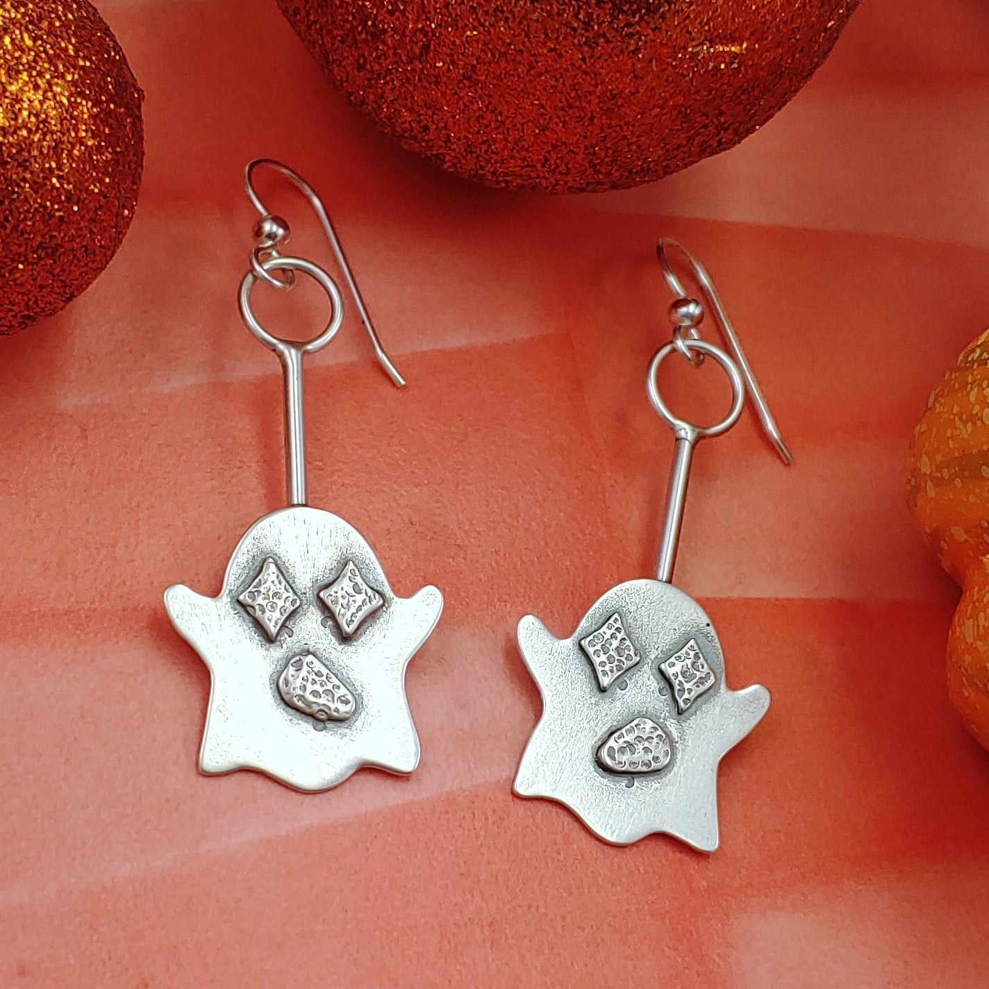 Cute sterling silver ghost earrings with stamped retro star shaped eyes on an orange background.