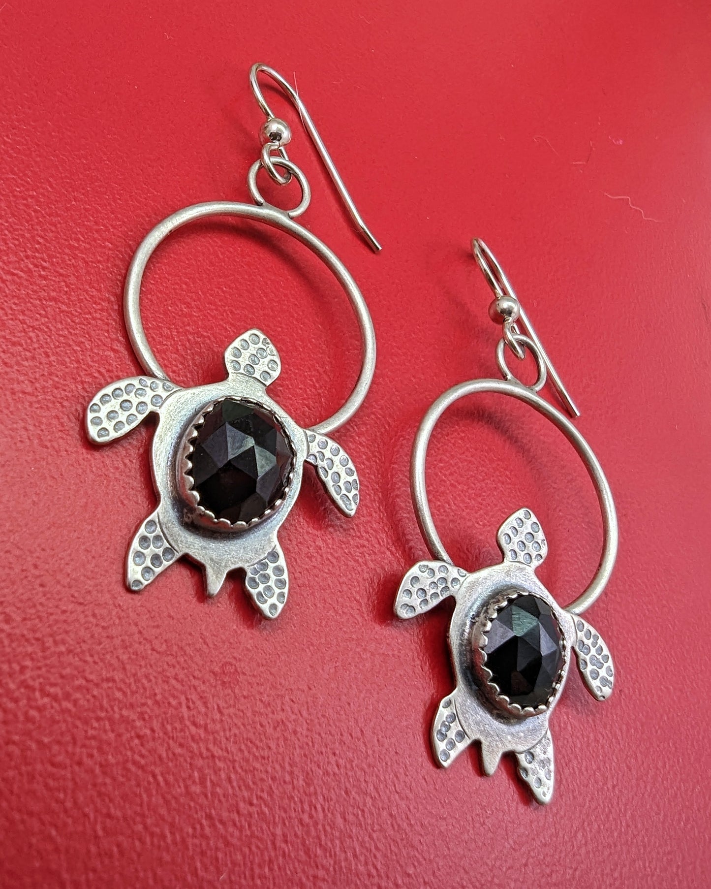Sterling silver handmade earrings with rosecut black onyx on red background shot sideways