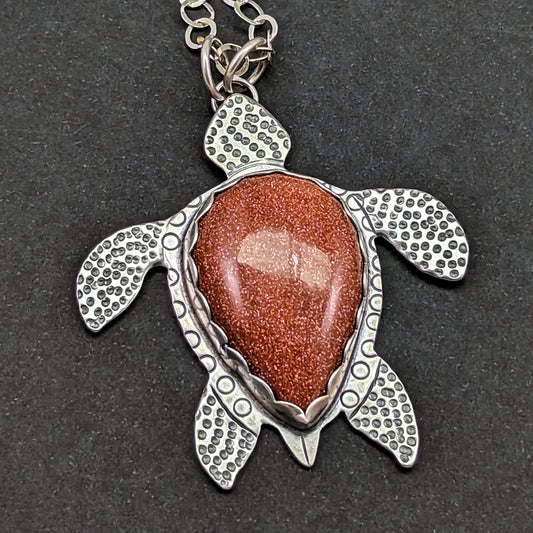 Sterling silver handmade sea turtle necklace with goldstone on black background