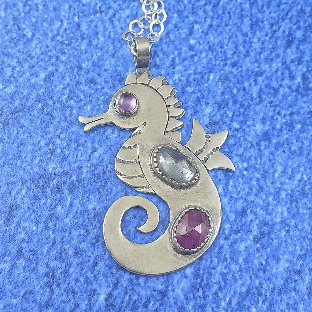 Sterling silver handmade seahorse with rosecut danburite and ruby with pink cubic zirconia eye on blue background