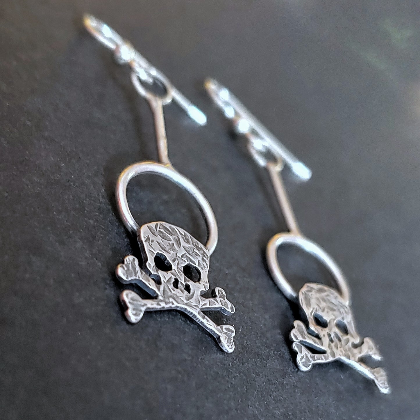 Close up view of the hammered sterling silver skull earrings on a black background.