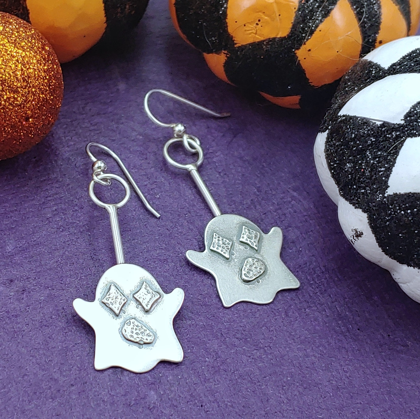 Cute sterling silver ghost dangle earrings with retro star shaped eyes on a purple background surrounded by little colorful pumpkins.