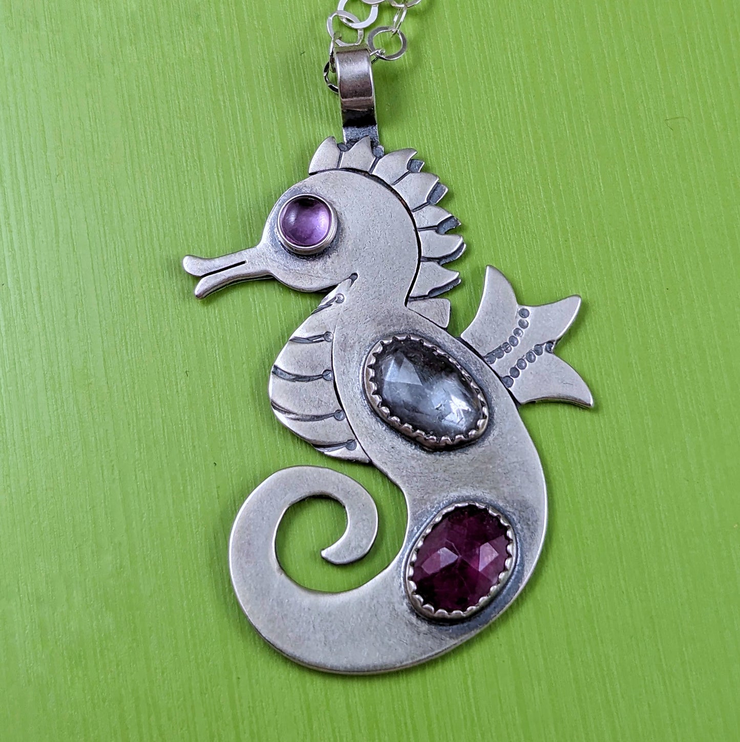 Sterling silver handmade seahorse with rosecut danburite and ruby with pink cubic zirconia eye on a green background