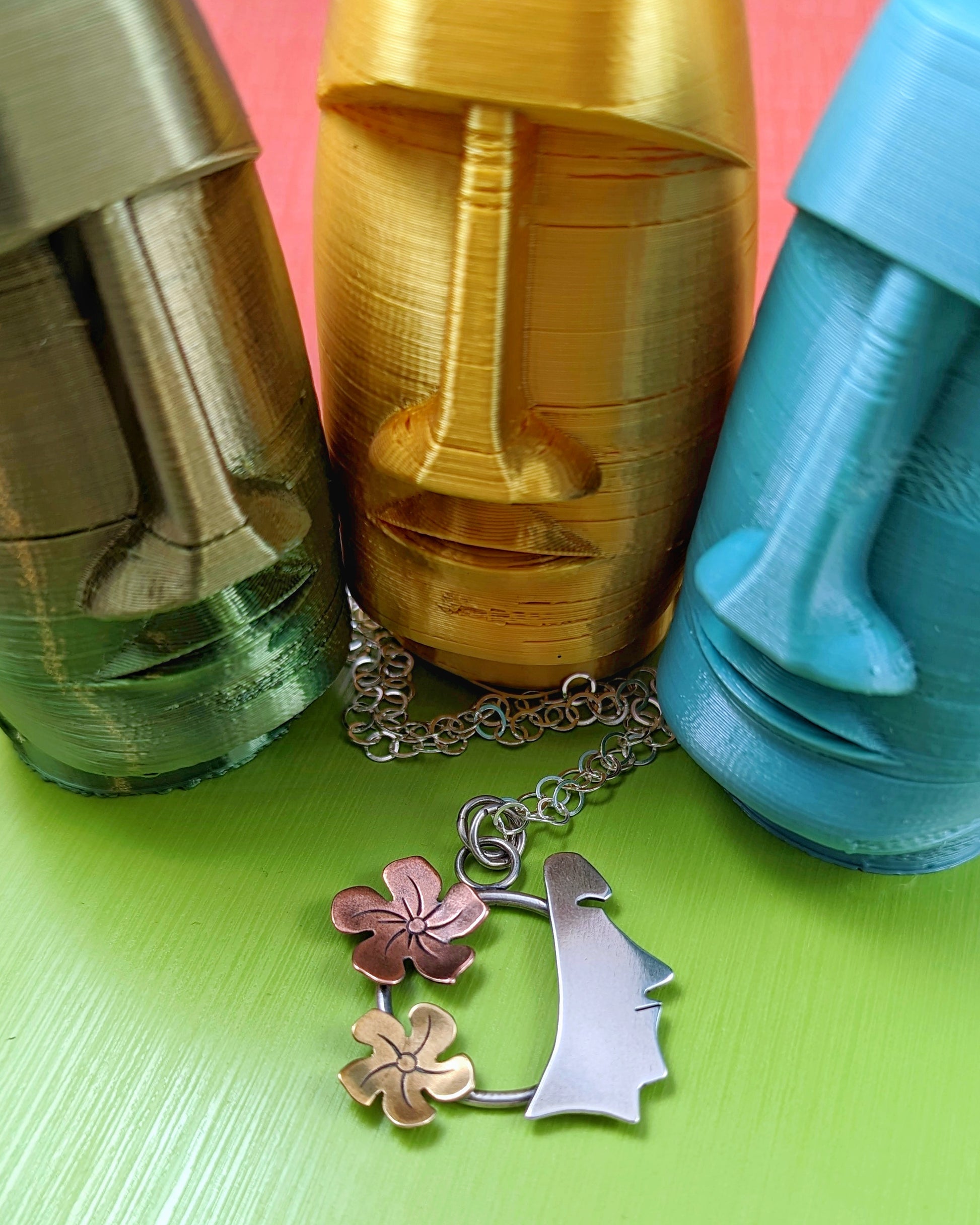Sterling silver, copper, and brass necklace on green background with moai statues