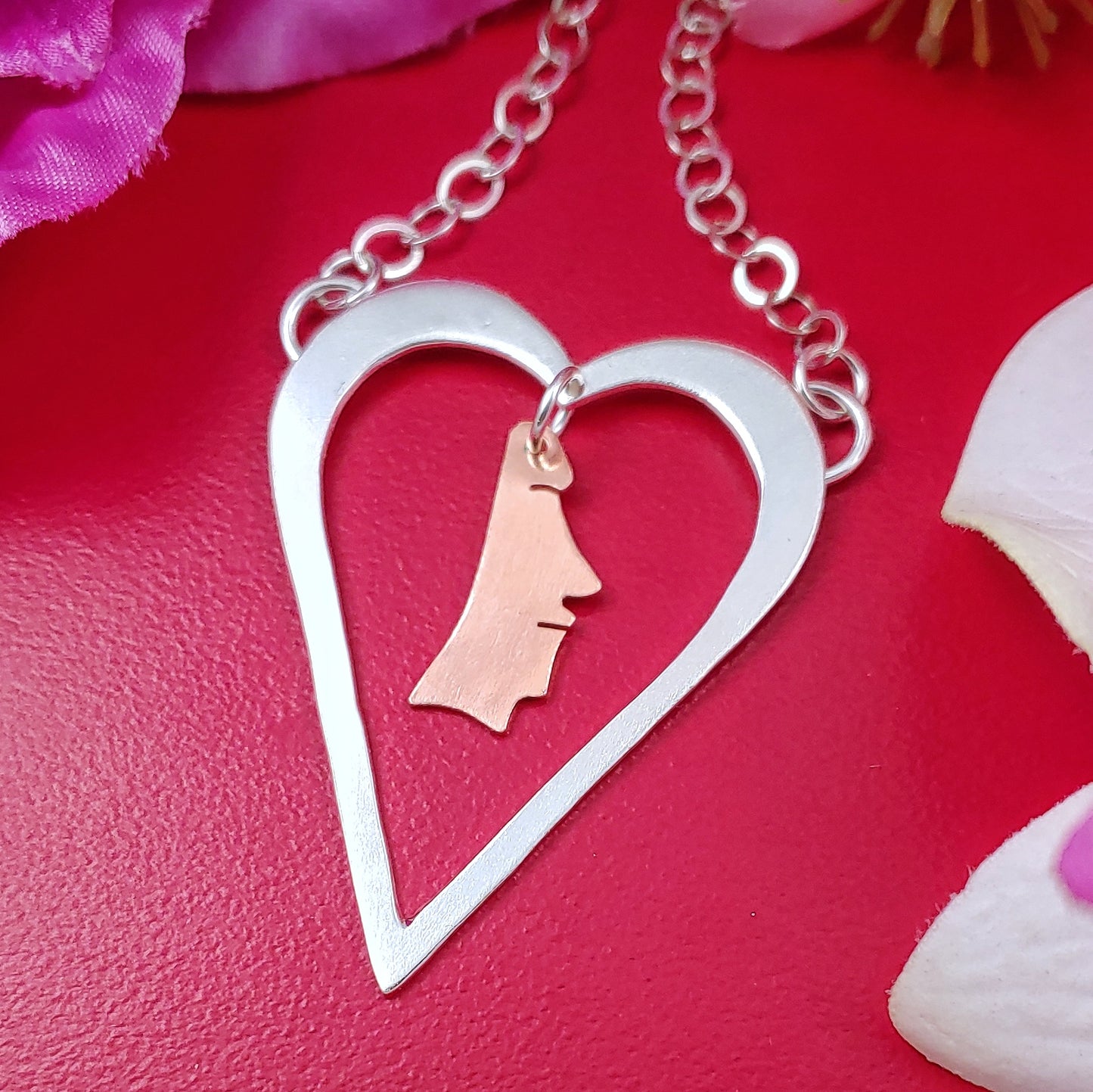 Sterling silver heart shaped necklace with a copper moai head dangling from the middle