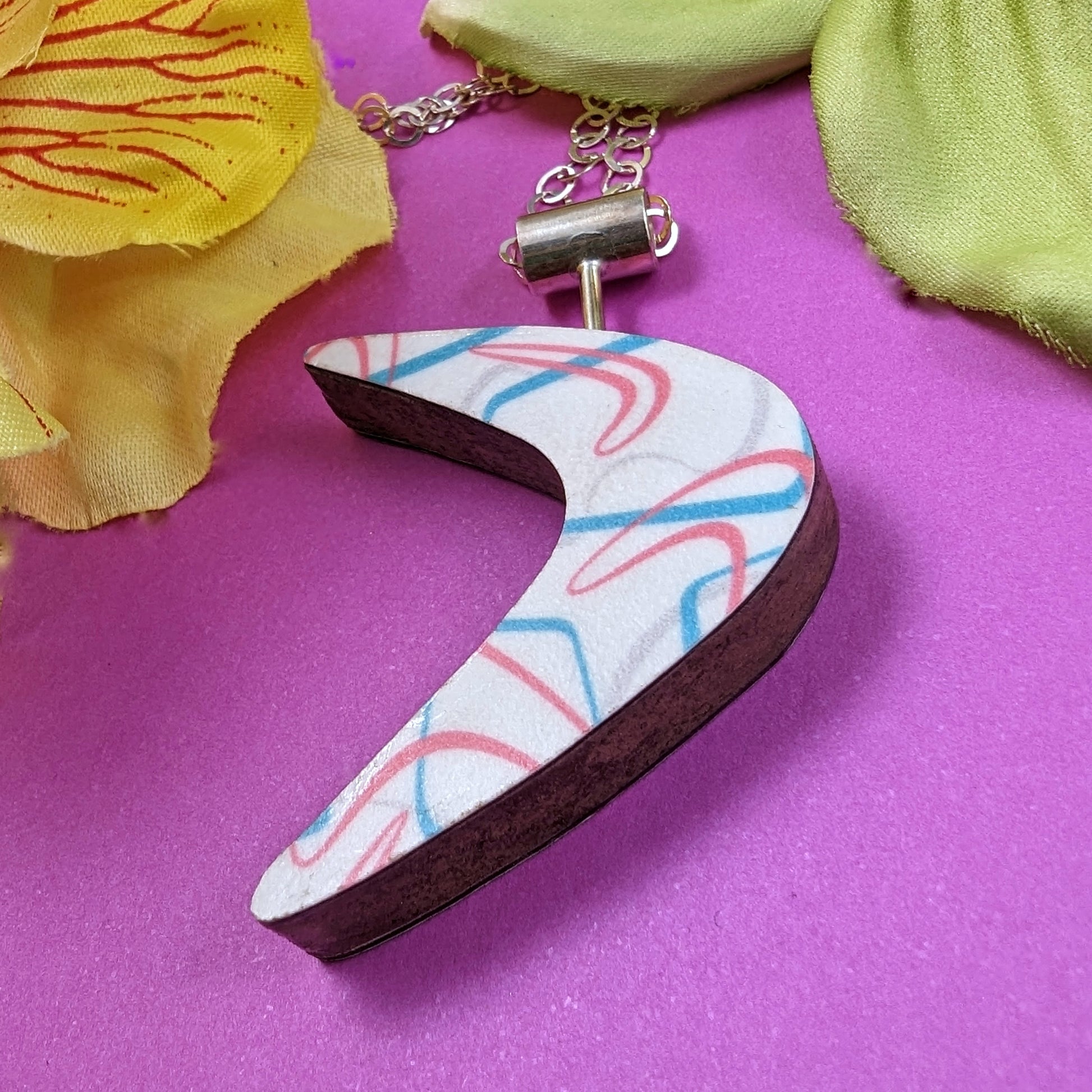 Boomerang shaped laminate on wood necklace on pink background